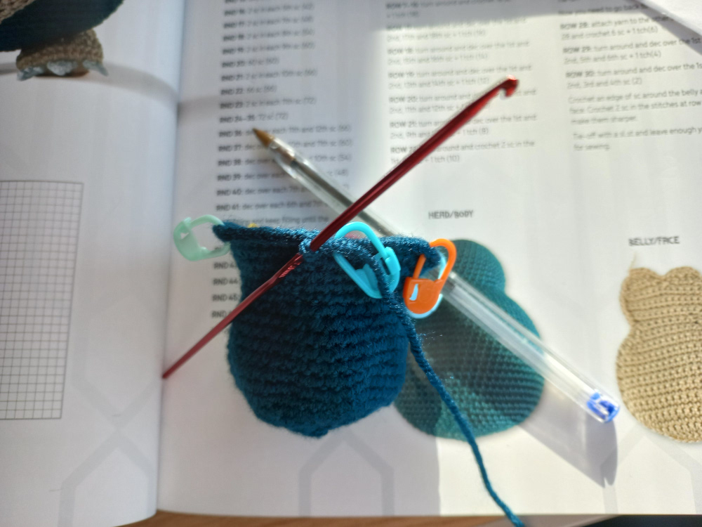 A crochet project featuring several stitch markers (beginning of a Snorlax from Lee Sartori&rsquo;s Pokemon crochet book)
